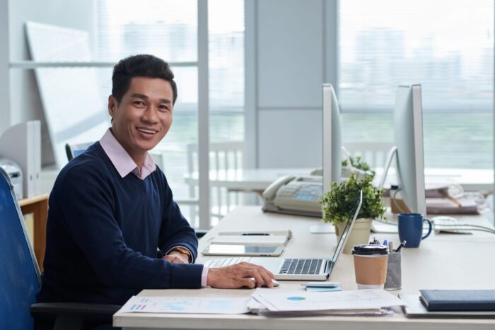 Photo of smiling man in office illustrates blog "Is Factoring a Short-Term or Long-Term Solution?"
