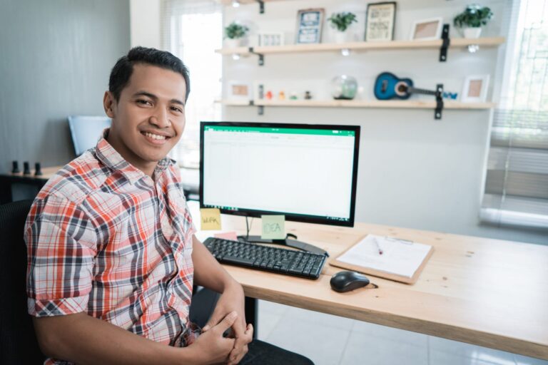 Photo of smiling man in front of computer illustrates blog: "How to Handle Past-Due Invoices"