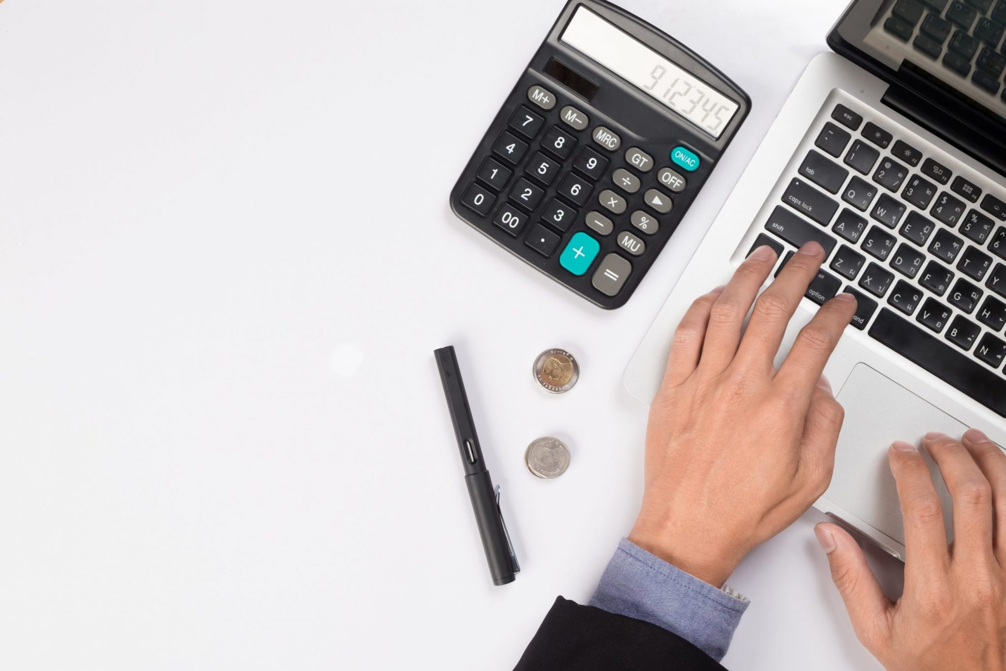 Photo of man writing on laptop with calculator beside him illustrates blog: "How Factoring Can Help Your Business Deal With the Effects of Inflation"