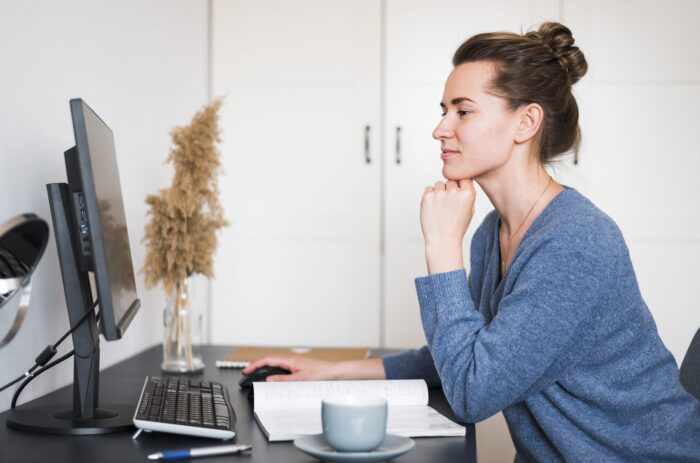 Woman sitting at desk looking at computer illustrates blog "Do Factoring Companies Check Your Credit?"