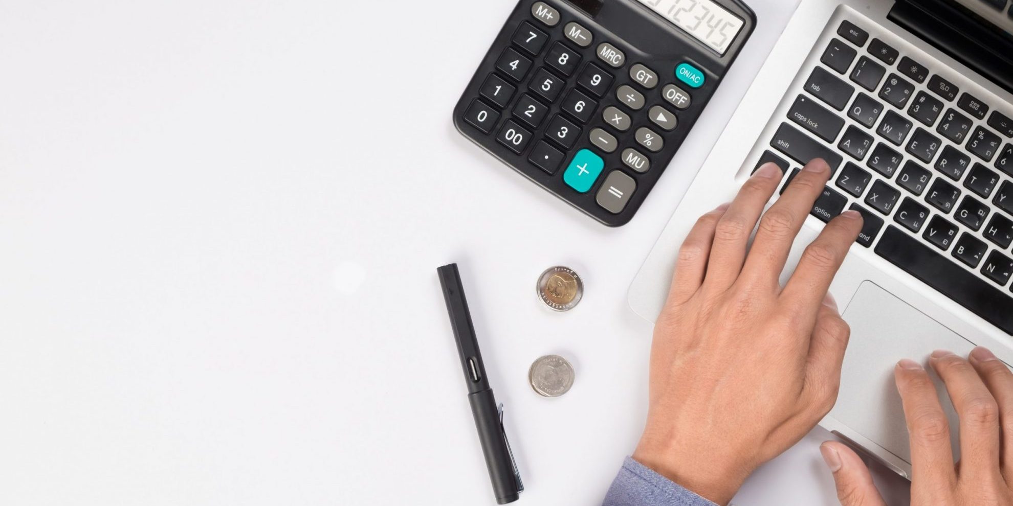 Photo of man writing on laptop with calculator beside him illustrates blog: "How Factoring Can Help Your Business Deal With the Effects of Inflation"