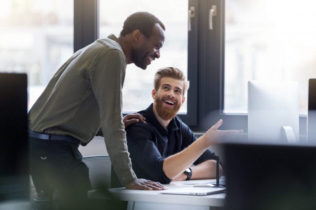 Photo of two smiling men at work illustrates blog: "How Do You Qualify for Receivables Factoring?"