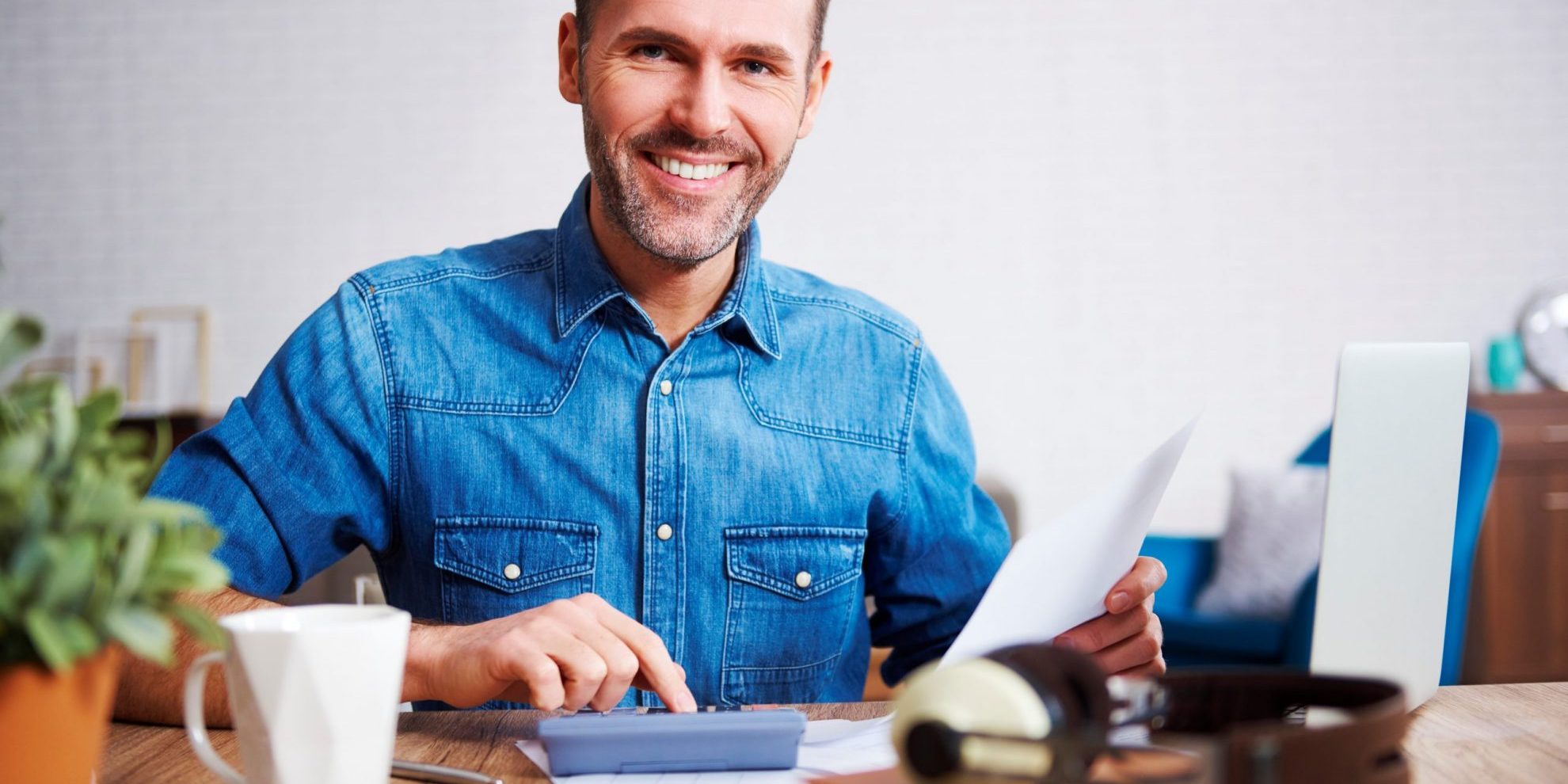 Photo of man smiling with invoices and calculator illustrates blog: "Invoice Management: 5 Tips for Small Businesses"