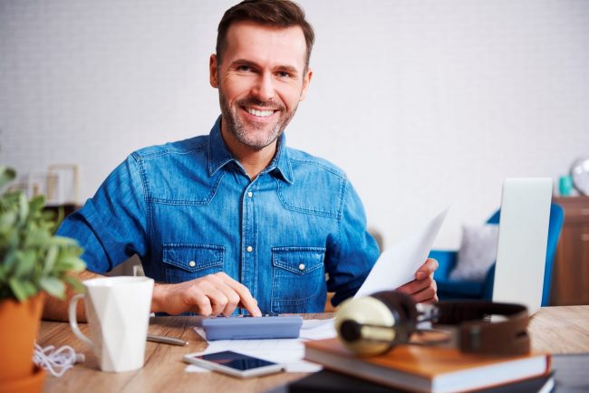 Photo of man smiling with invoices and calculator illustrates blog: "Invoice Management: 5 Tips for Small Businesses"