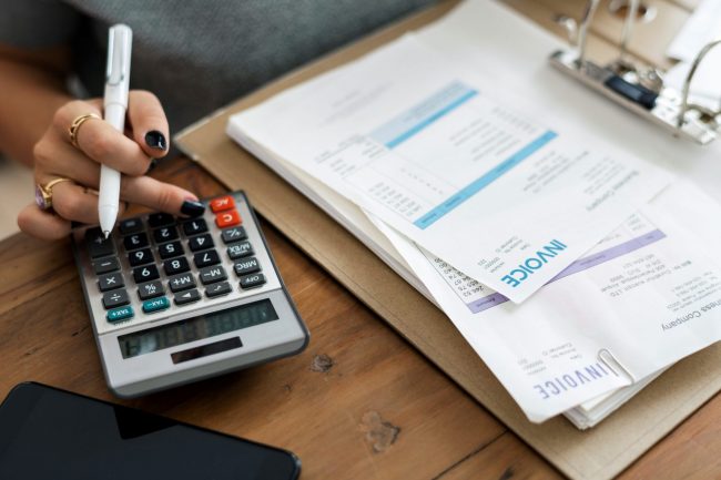 Closeup desk with invoice and calculator illustrates blog: "Receivables Factoring vs Forfaiting: What Is the Difference?"