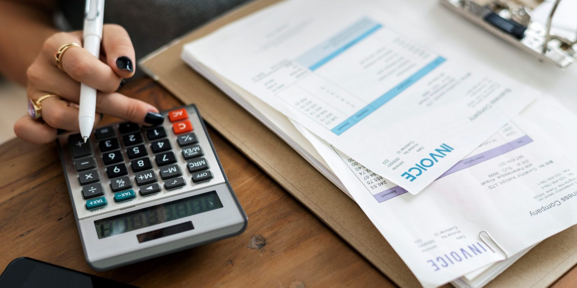 Photo of person with invoices and calculator illustrates blog: " Types of Factoring: Which One Works for You?"