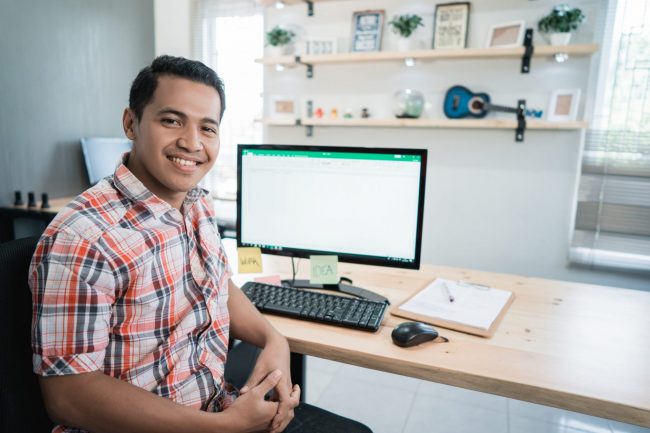 Photo of smiling man in front of computer illustrates blog: "How to Handle Past-Due Invoices"