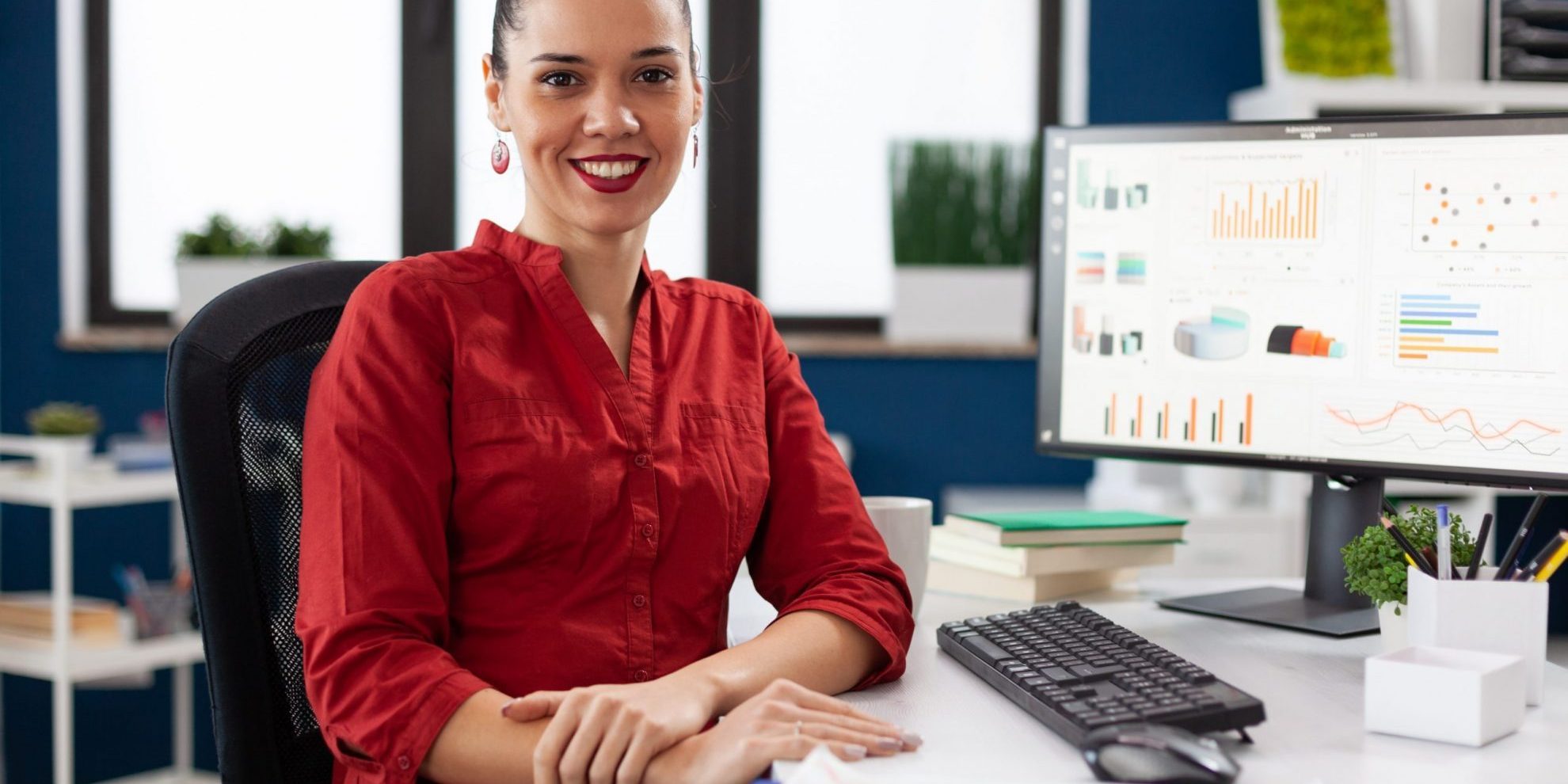 Smiling woman in office sitting at desk with computer screen illustrates blog "Accounts Receivable vs Control Account: What Is the Difference?"