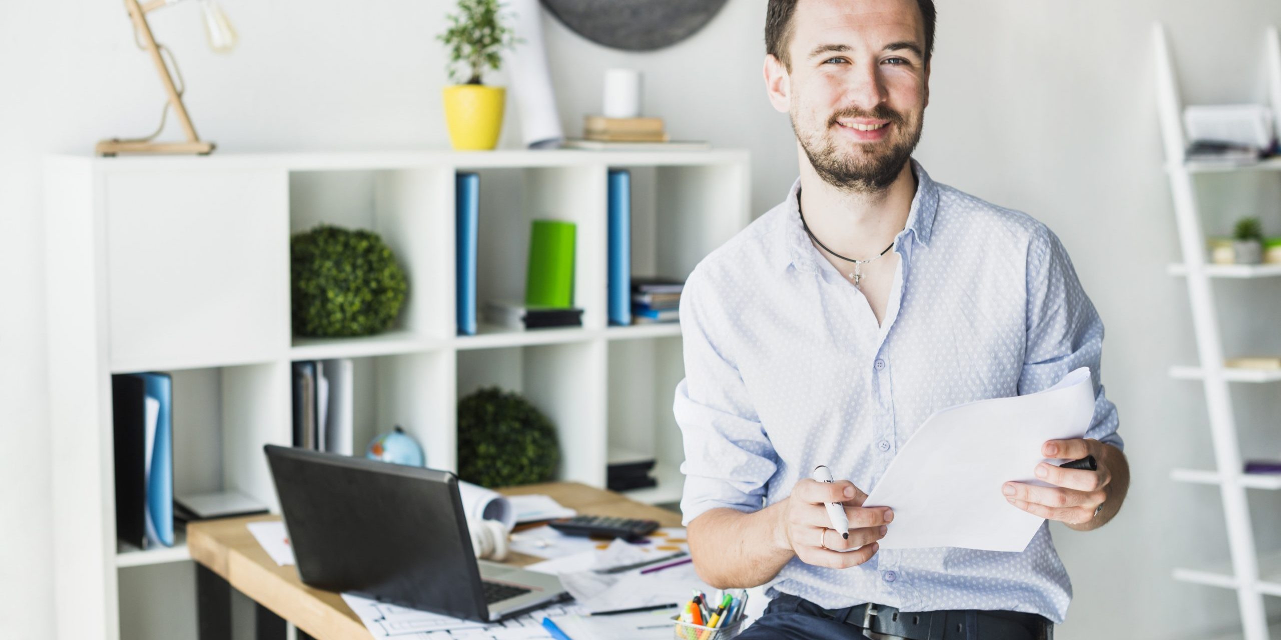 Smiling man in office holding papers illustrates blog "Invoice Factoring vs Overdraft: What Is the Difference?"