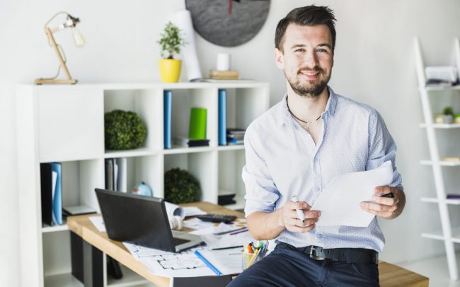 Smiling man in office holding papers illustrates blog "Invoice Factoring vs Overdraft: What Is the Difference?"