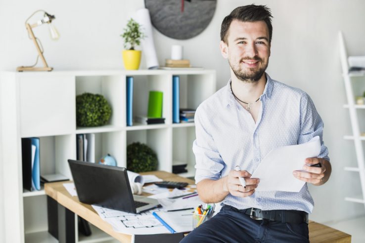 man-smiling-office-fp Smiling man in office holding papers illustrates blog "Invoice Factoring vs Overdraft: What Is the Difference?"